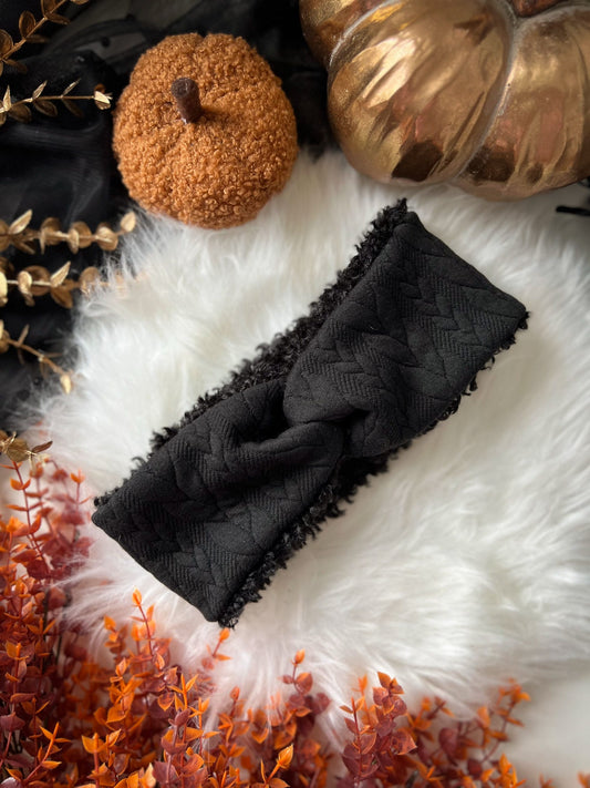 Black knit jersey headband on a textured white surface with decorative pumpkins and gold leaves.