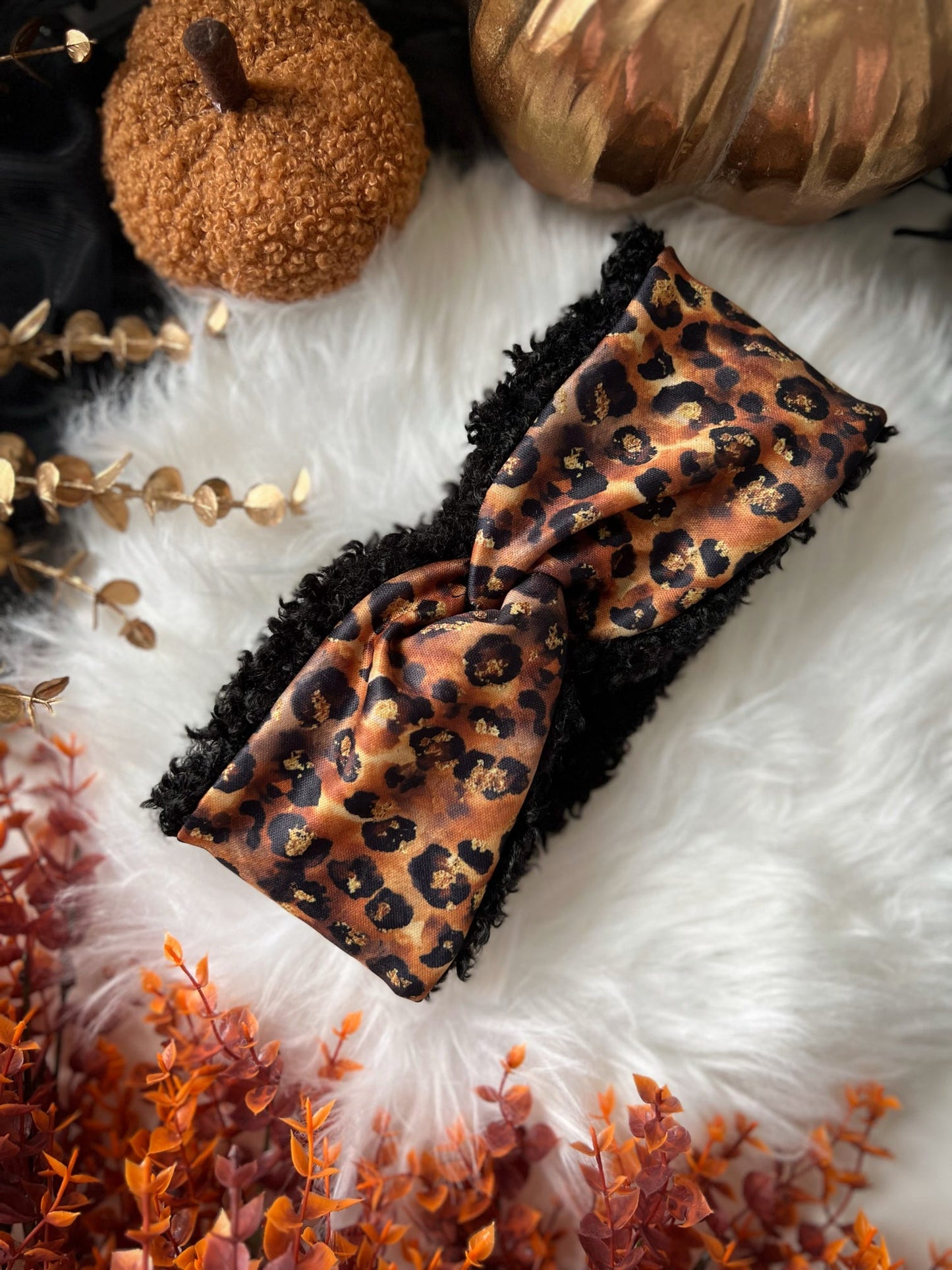 Leopard print headband on a white fur surface with pumpkins and gold leaves.