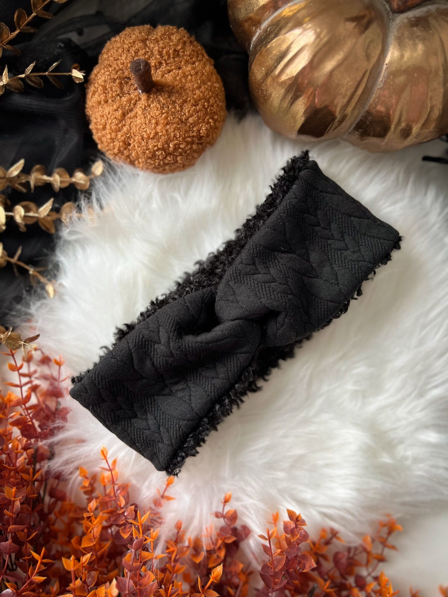 Black knit jersey headband on a textured white surface with decorative pumpkins and gold leaves.