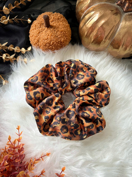 Leopard print scrunchie on a fluffy white surface with decorative pumpkins and gold leaves.
