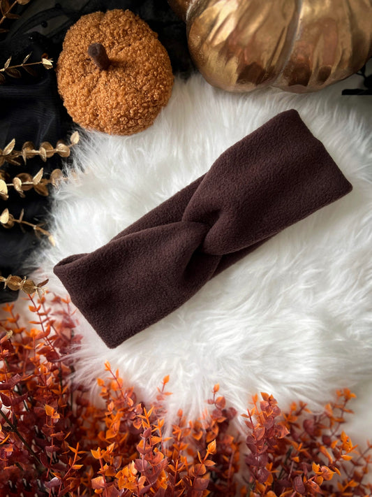 Brown knotted polar fleece headband on a white fur surface with autumn-themed decorations.