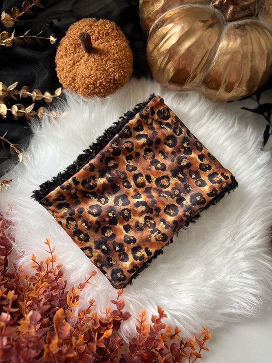 Leopard print dog snood on a white fur surface with decorative elements.