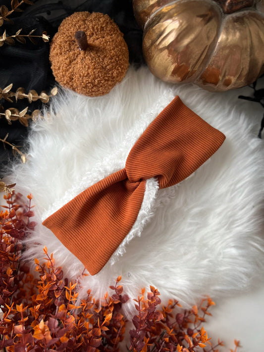 Orange hair band on a white fur surface with pumpkins and dried flowers.