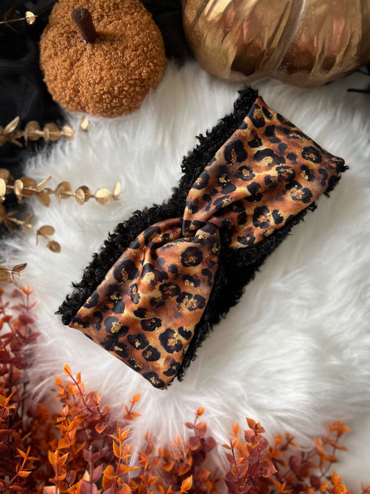 Leopard print headband on a white fur surface with pumpkins and gold leaves.