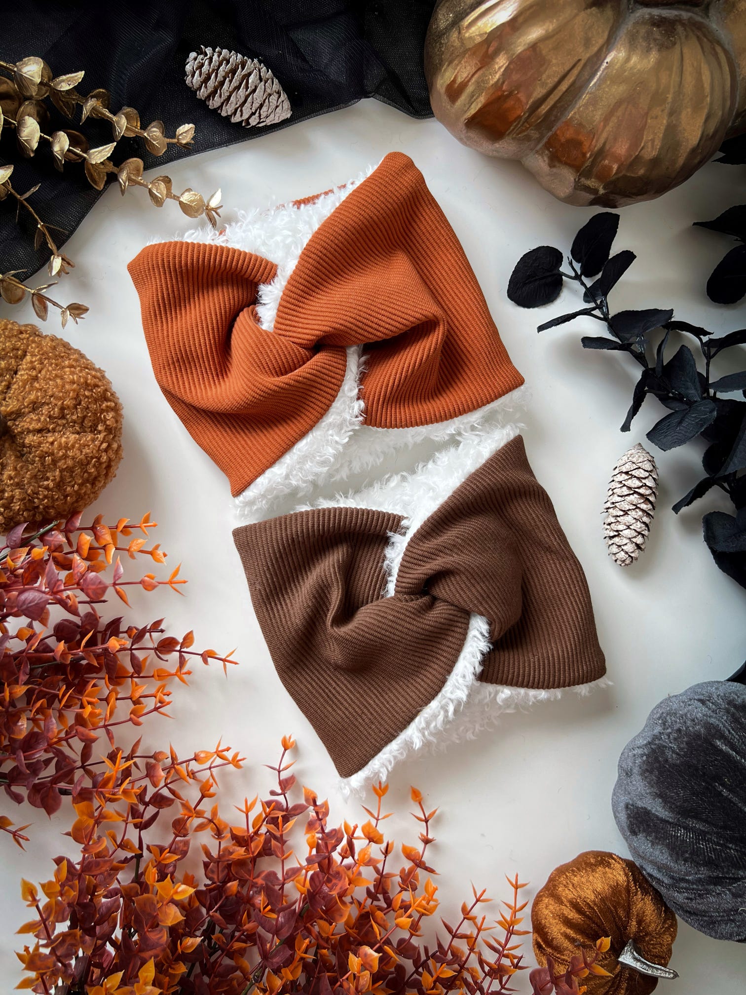 Brown and orange twist dog snoods on a white surface with decorative pumpkins and leaves.