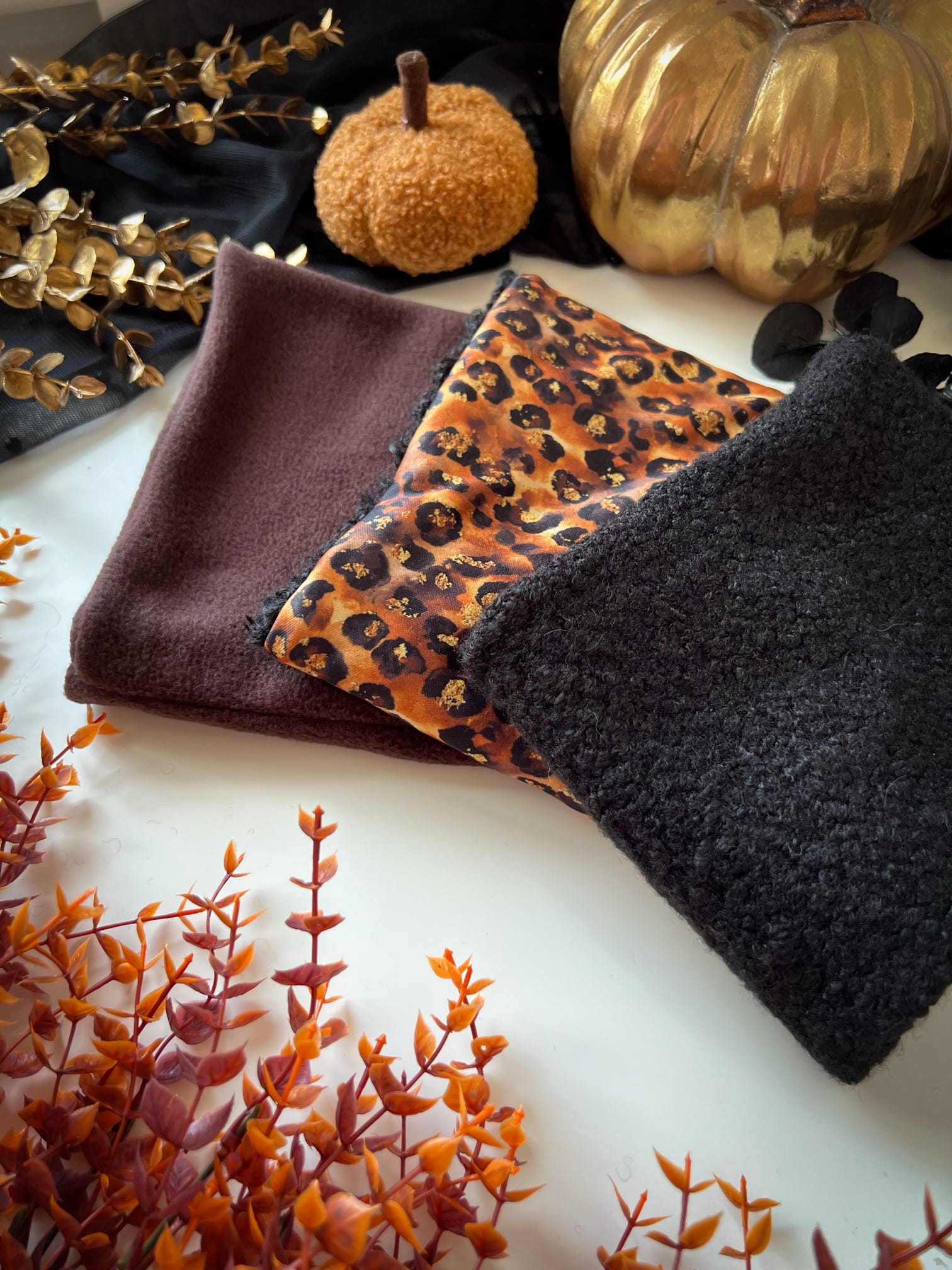 Three dog snoods  in brown, leopard print, and black on a white surface with decorative elements.