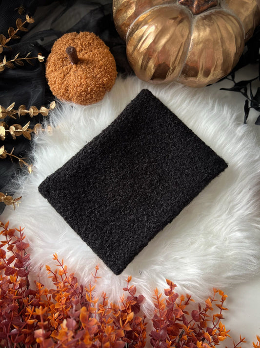 Black dog snood on a white surface with pumpkins and autumn leaves in the background
