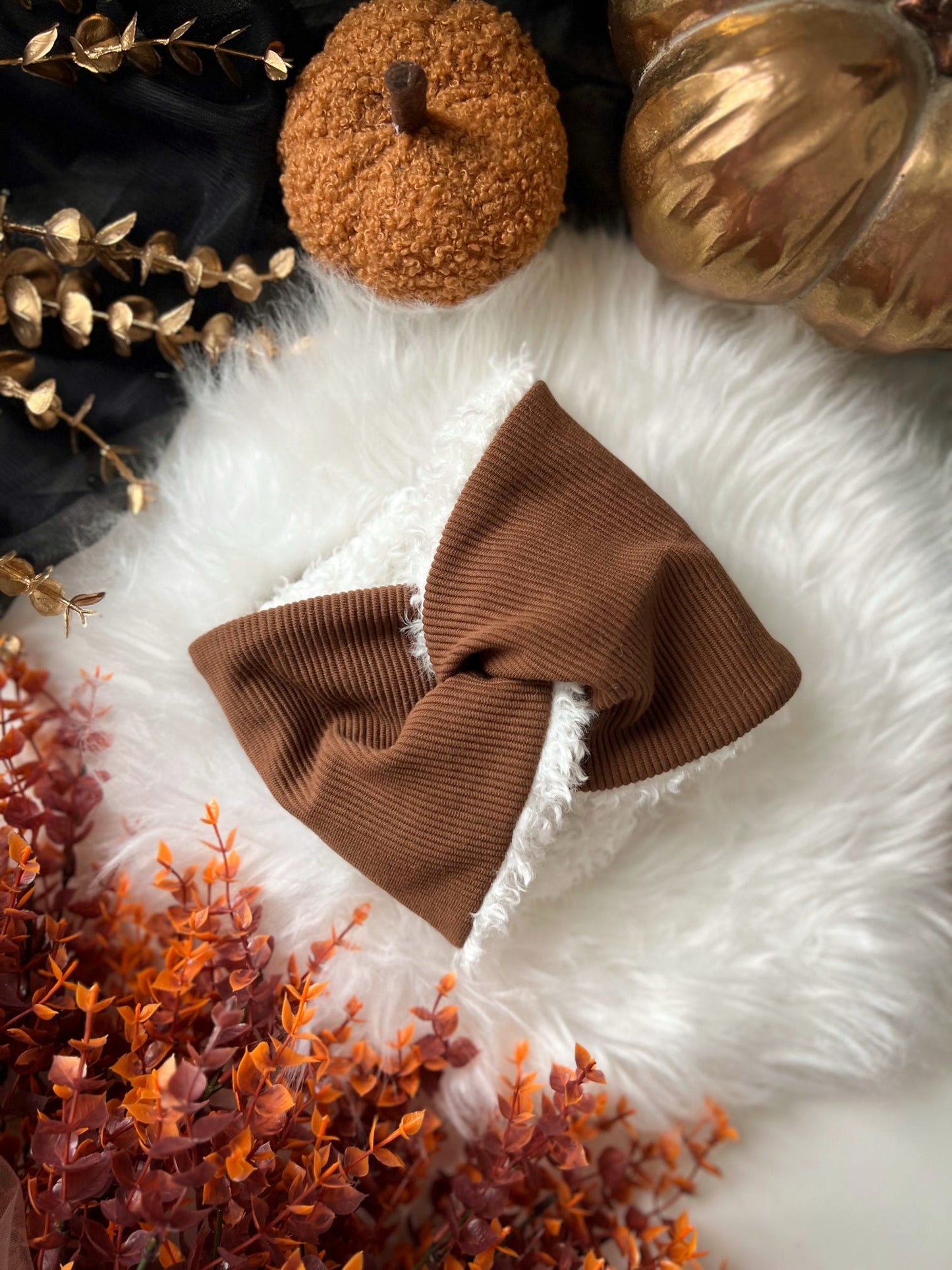 Brown knitted dog snood on a white surface with decorative pumpkins and plants.