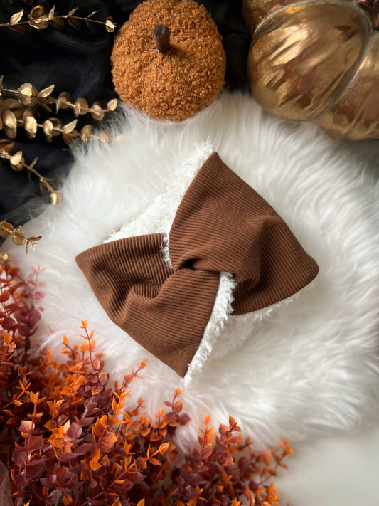 Brown knitted dog snood on a white surface with decorative pumpkins and plants.